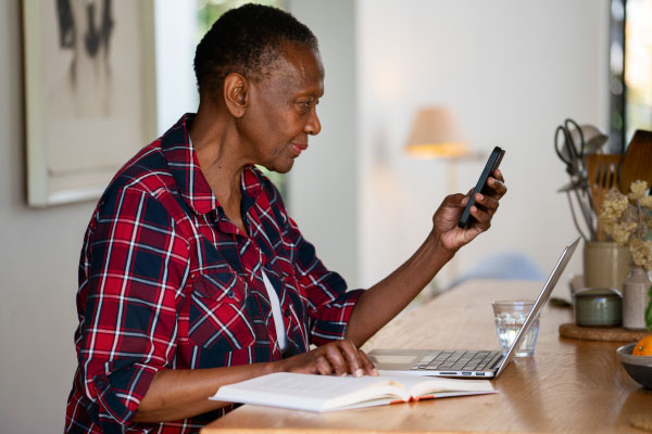 senior woman holding phone and looking at computer